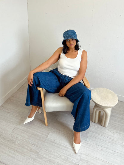 Woman sitting on a chair wearing a white top, blue jeans, and a blue hat in a minimalistic room.